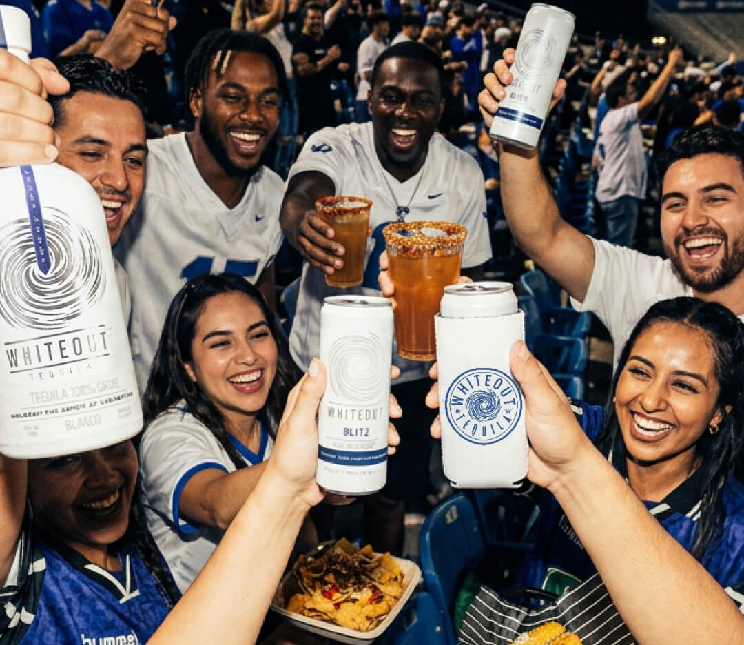 People at a sports event holding Whiteout drinks and smiling.