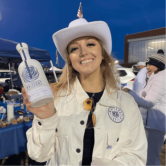 Woman in a white cowboy hat holding a bottle of whiteout at an outdoor event.