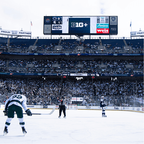 Hockey game in progress with players on the ice and a large scoreboard in the background.