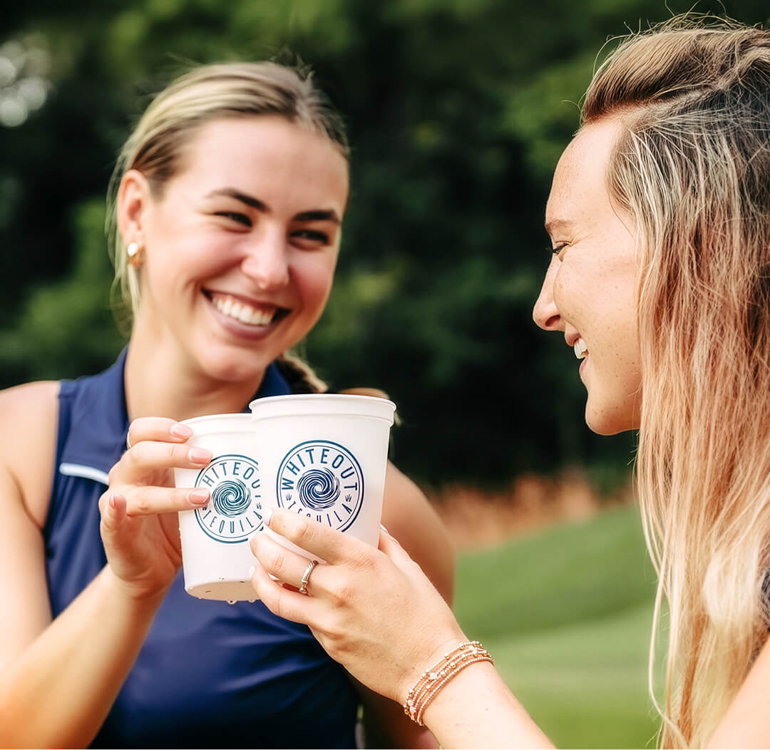 Two women holding Whiteout cups with drinks outdoors